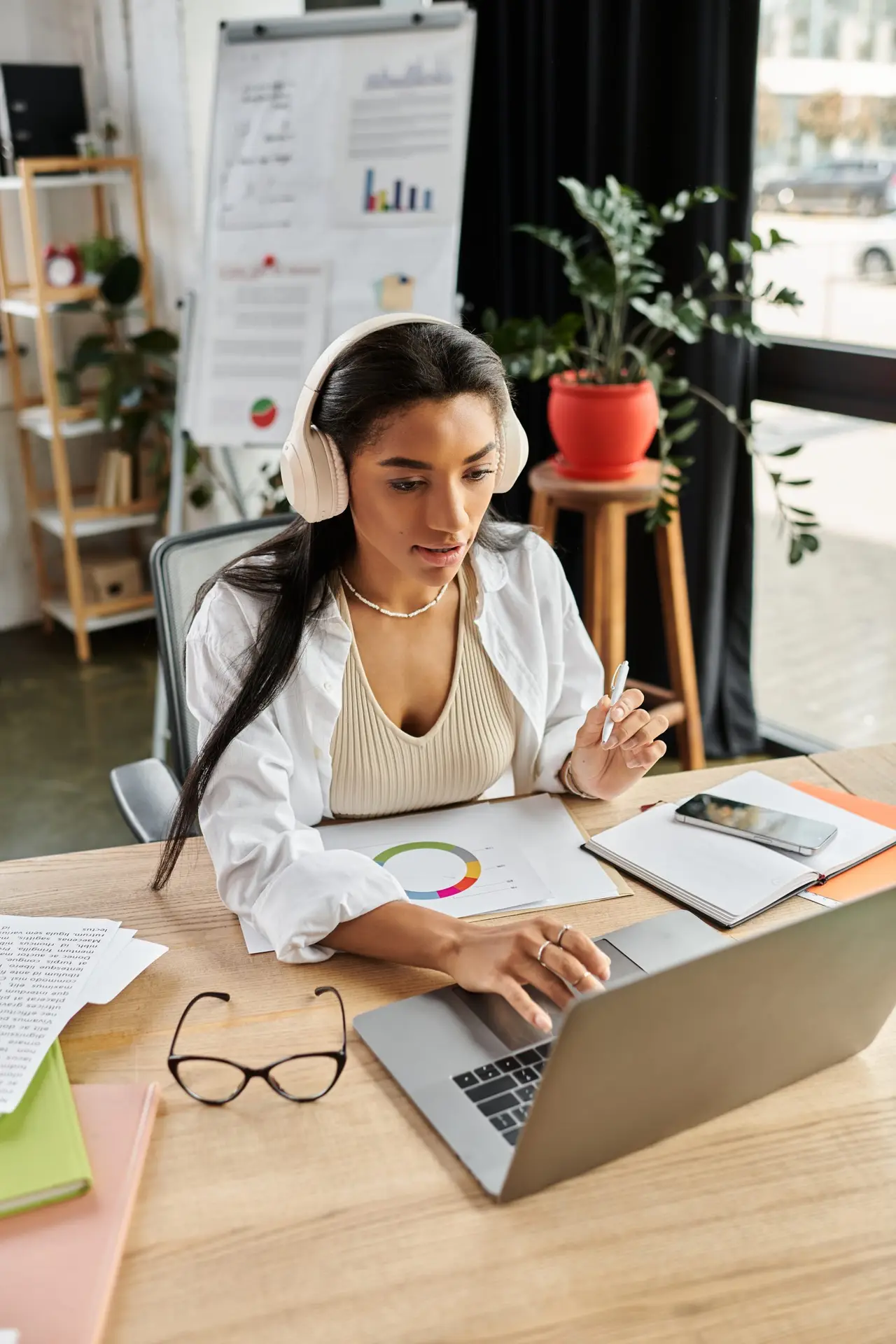 A young woman engages in work at her desk, analyzing data and wearing headphones.